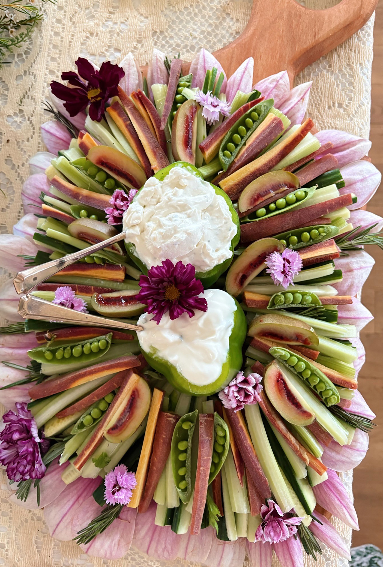 vegetable platter with edible flowers placed on veggies with dip in peppers in the middle of the vegetables